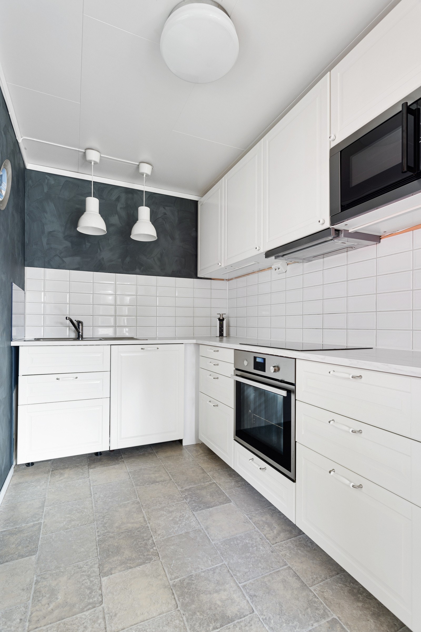 Lys, fin kjøkkeninnredning av hvitmalte profilerte fronter. Benkeplate av laminat med flisvegg mellom benke- og overskaper. Galleribilde