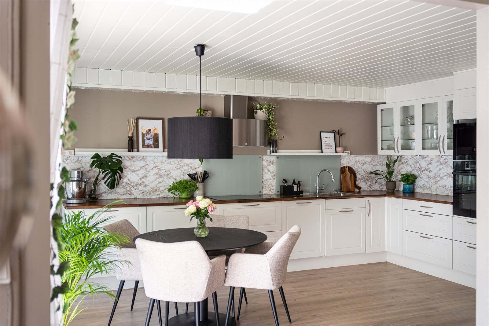 Skap og skuffer har hvite profilfronter, mens overskapene har vitrinedører. Benkeplatene er i treimitert laminat og veggene bak har marmorfolie. Foto: Hilde Hugsand. Galleribilde