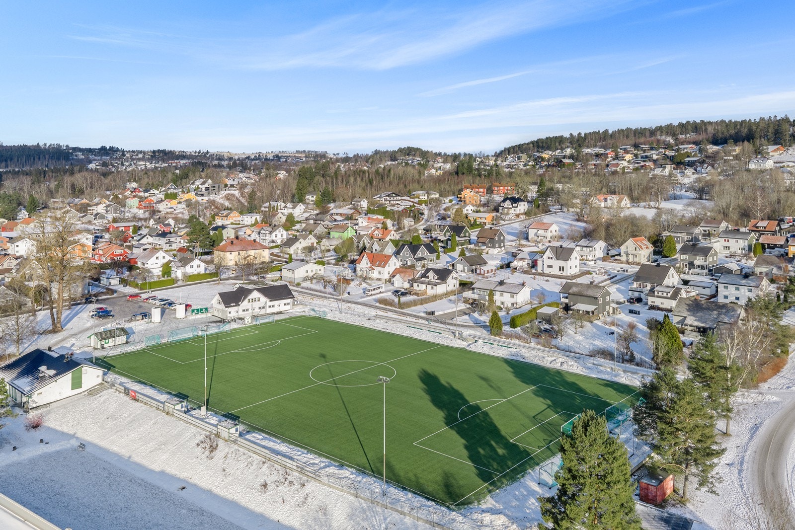 Fotballbane med kunstgress i nærheten av boligområdet, omgitt av boliger og skog. Galleribilde