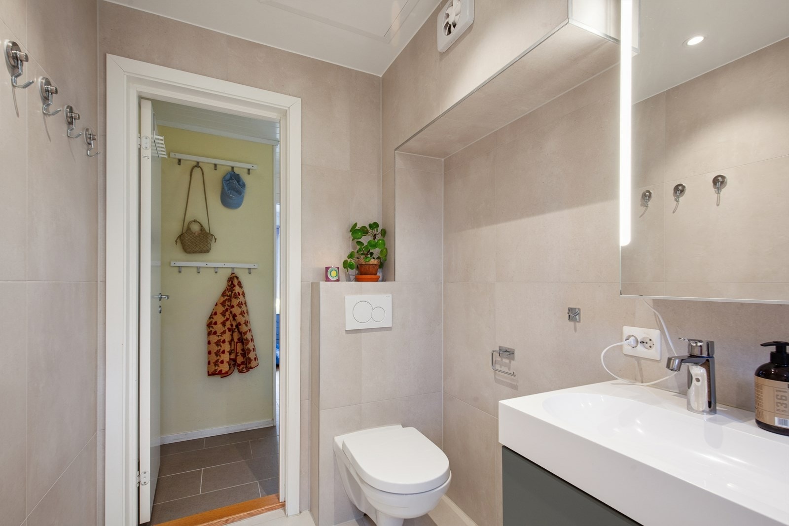 Badet er innredet med et vegghengt toalett og et badekar med dusj og glassvegg, baderomsinnredning med servant, samt speilskap med belysning. Galleribilde