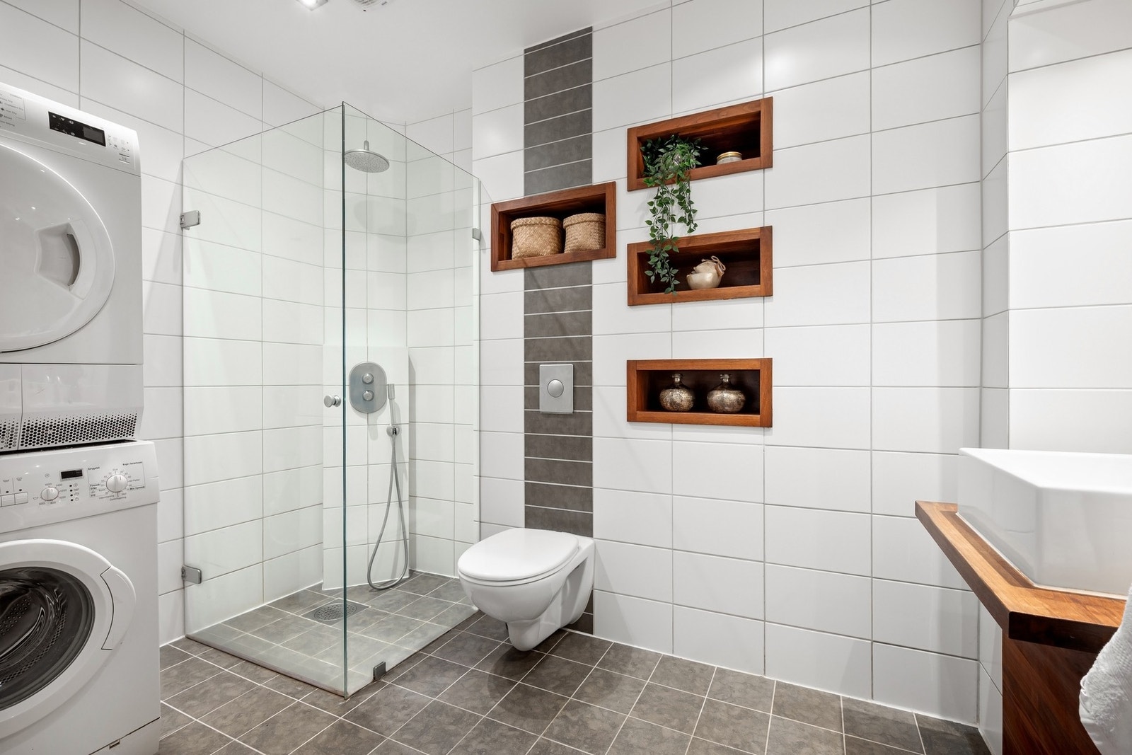 Romslig baderom med dusjhjørne med innfellbare glassdører, utstyrt med både regnfallsdusj og hånddusj - Vegghengt klosett. Galleribilde