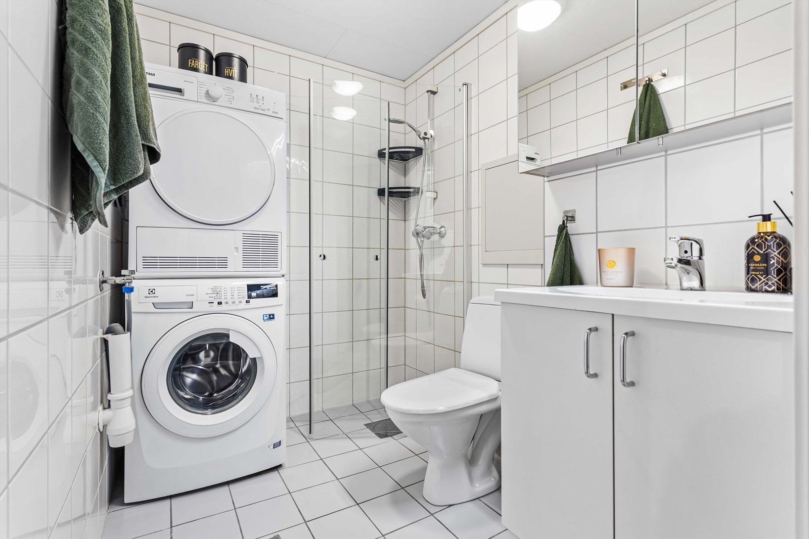 Lyst, flislagt baderom med servantinnredning og speilskap. På badet er det dusjhjørne med innfellbare glassdører og toalett. Galleribilde