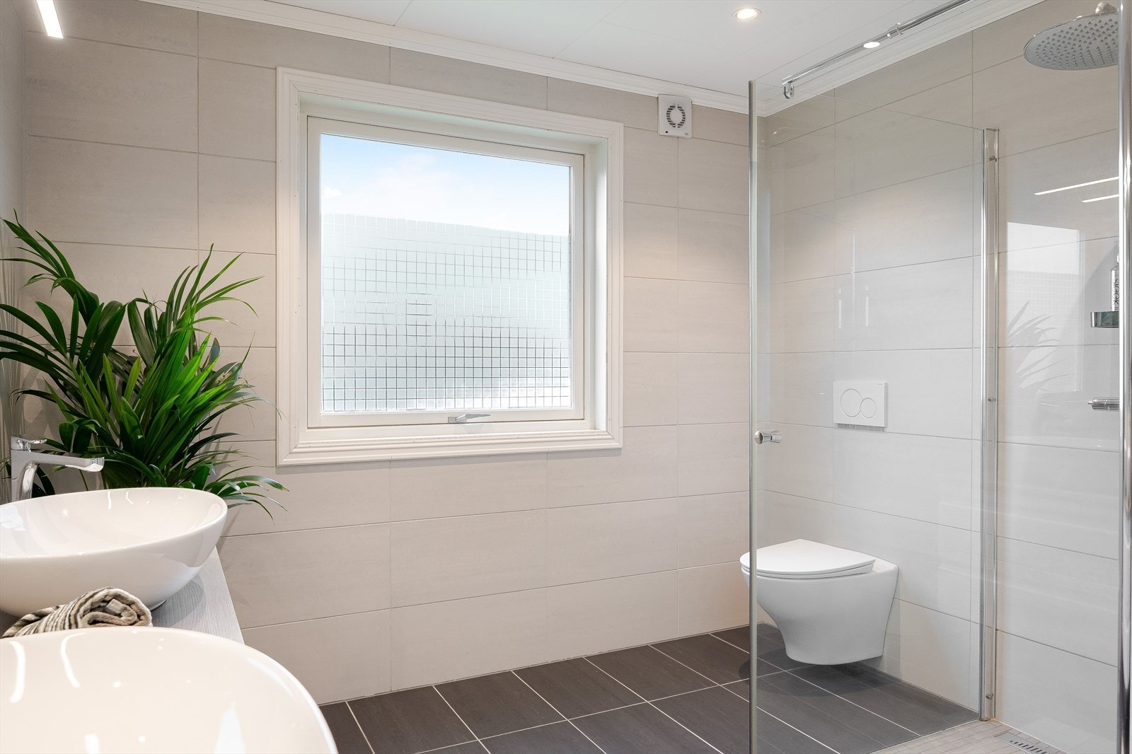 Baderommet er også utstyrt med dusjhjørne med glassdør og både hånd- og regnfallsdusj, samt vegghengt toalett. Galleribilde