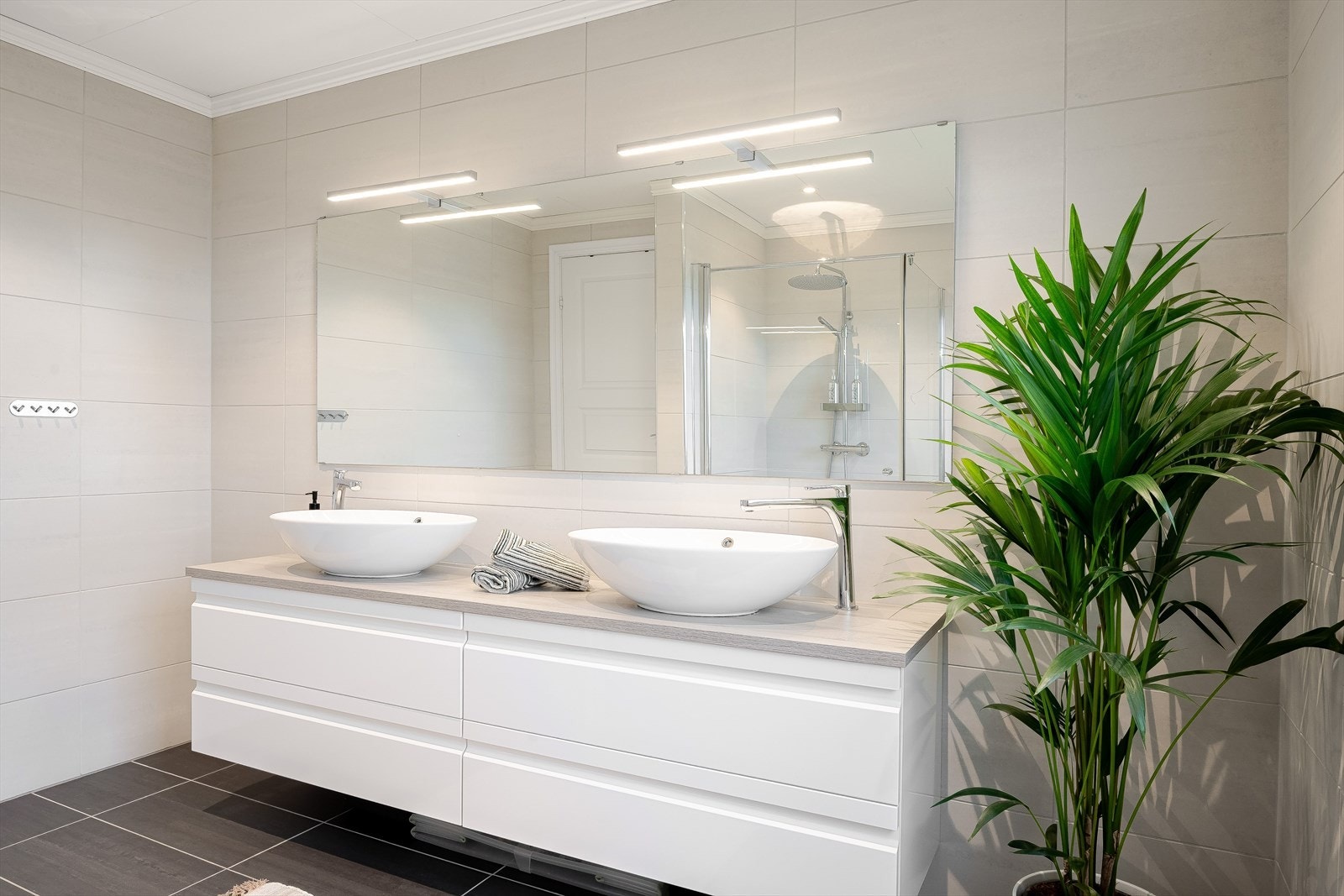 Moderne baderomsinnredning med skuffer og 2 ovenpåliggende bolleservanter, stort speil med belysning over. Galleribilde