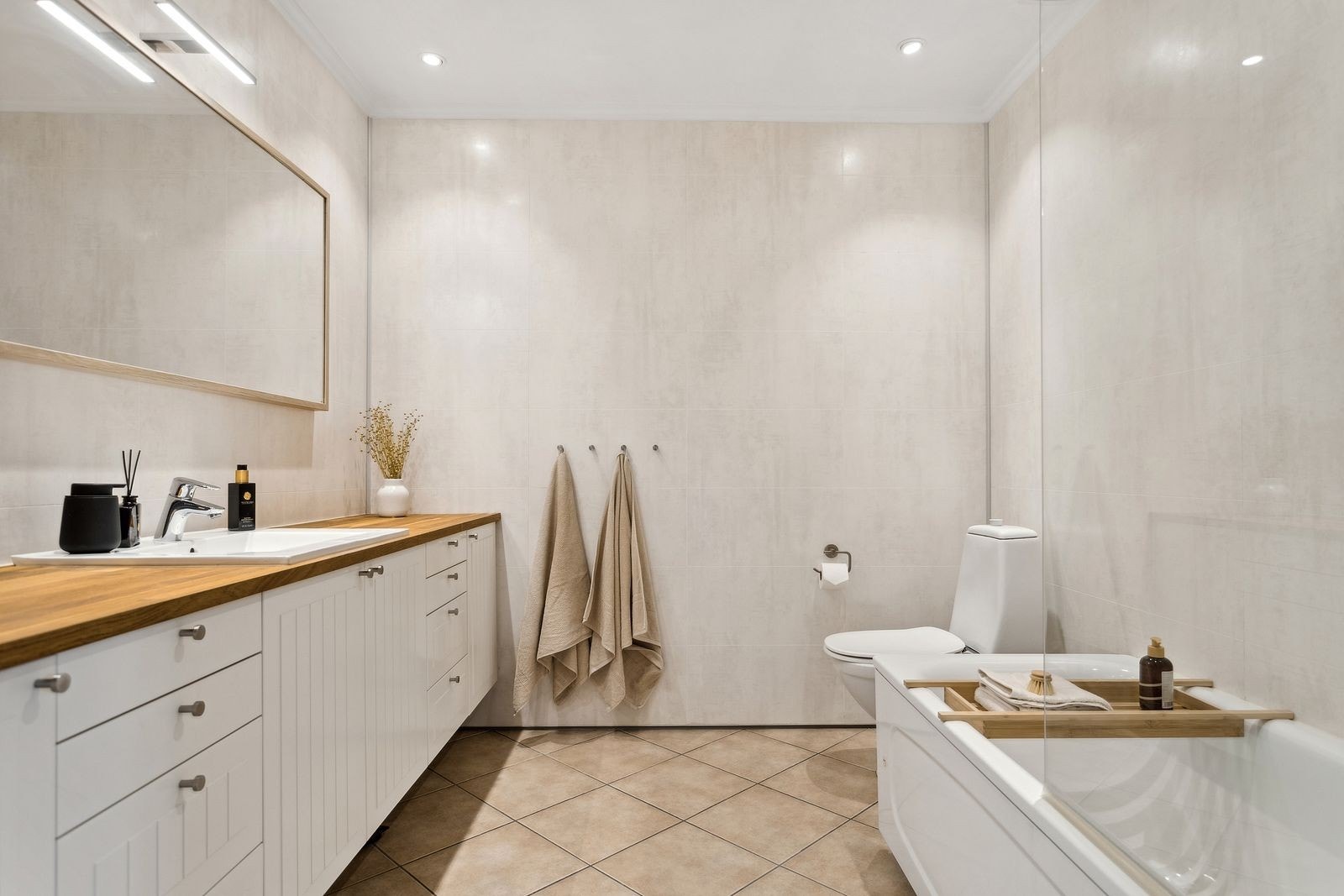 Baderommet måler 6 m² og er utstyrt med badekar med dusjdør, toalett, servant med underskap og speil. Galleribilde