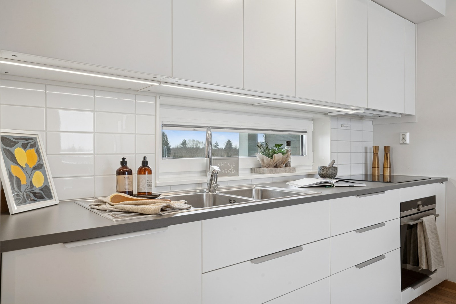 Kjøkkenet har lys under overskapene og fliser mellom benkeplate og overskap. Galleribilde