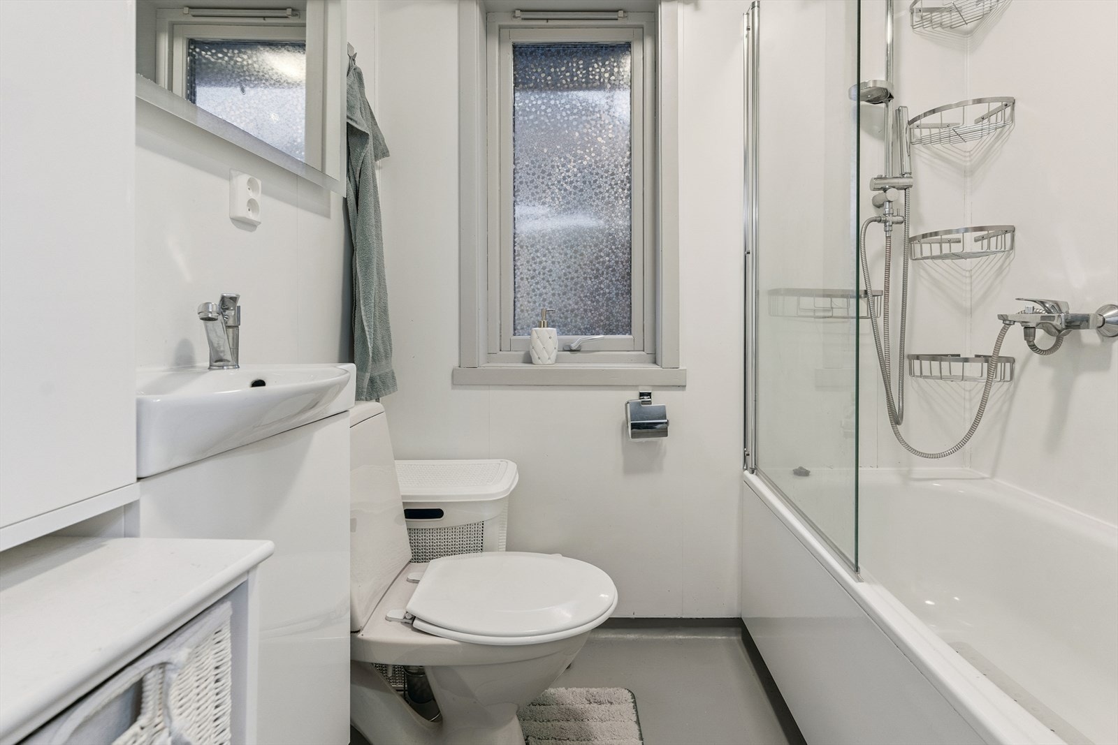 Baderom i 1.etasje. Rommet er frå byggeår, med belegg på golv, malte plater på vegg og himlingsplater. Av innreiing finn du badekar med dusj, servantinnreiing og golvståande toalett. Galleribilde