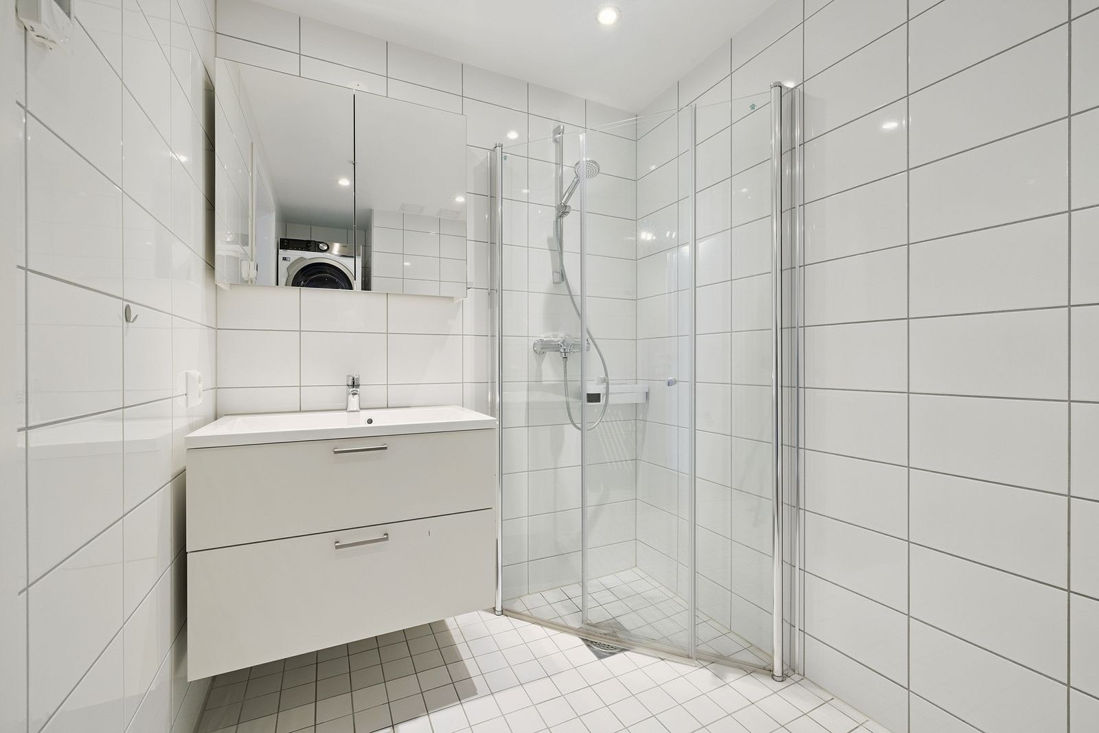 Flislagt bad med dusjhjørne i glass, servant med god oppbevaringsplass og moderne uttrykk. Galleribilde