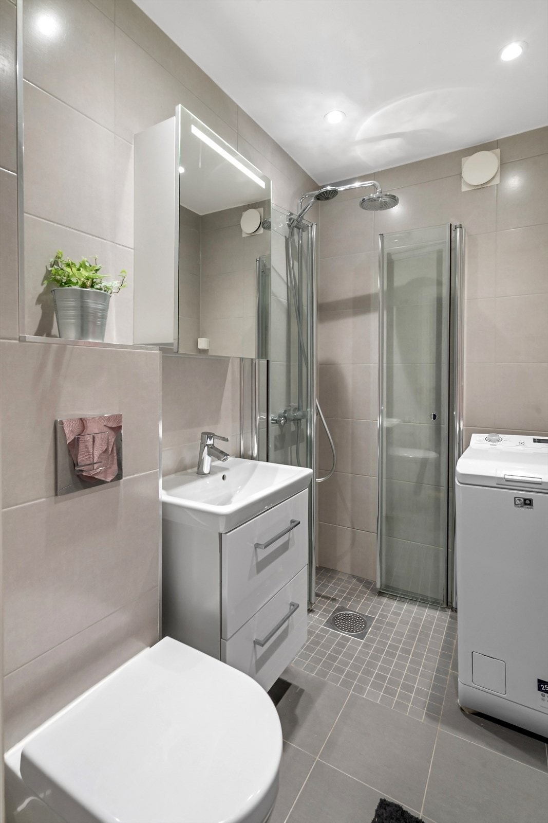 Utstyrt med regnfalldusj og innsvingbare dusjdører, servant med skuffer, veggmontert toalett og speilskap med lys. Galleribilde