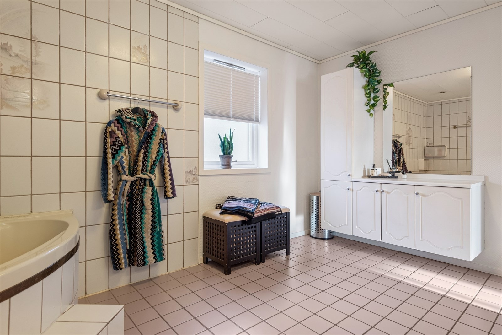 Det romslige baderommet i 1. etasje har flislagt gulv med varmekabler og veggfliser. Rommet er utstyrt med en stor baderomsinnredning med speil, samt et innfliset hjørnebadekar. Galleribilde