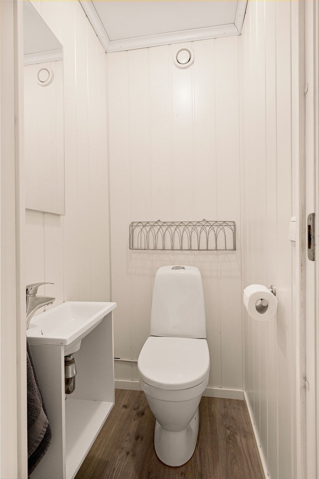 Toalettrom med laminat på gulv og vegger med mdf plater. Innredet med servant, speil og klosett. Galleribilde