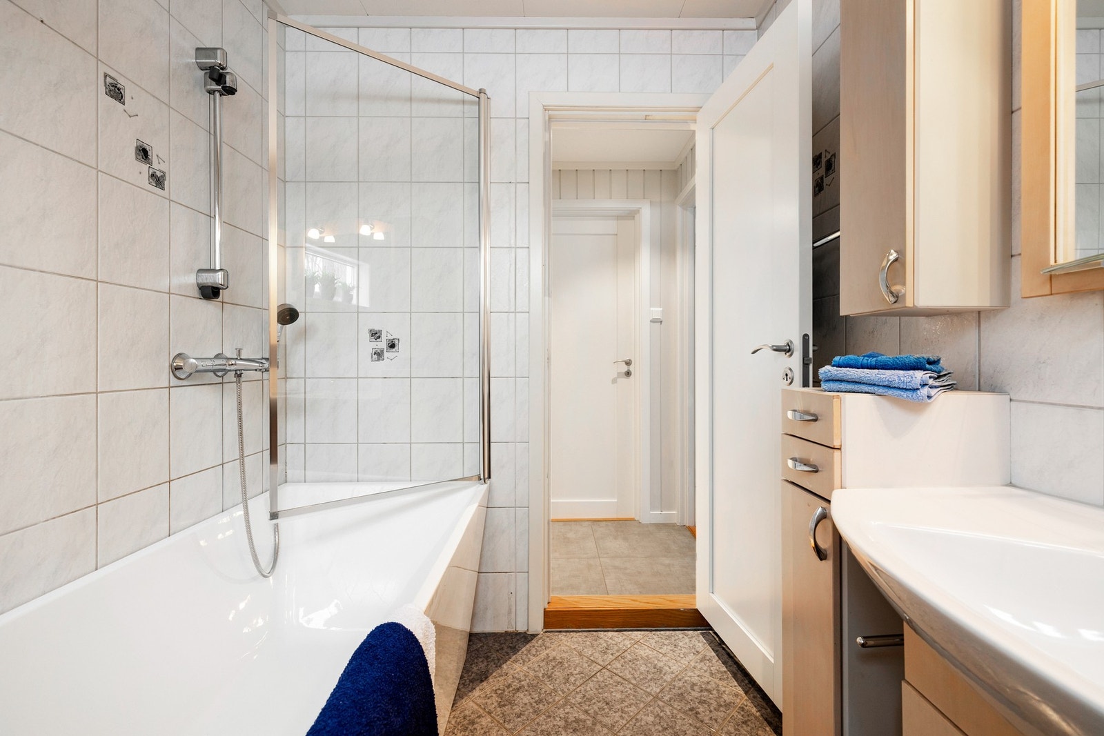 Badet har gulvstående toalett og badekar med dusj, og servant med skuffe- og skap innredning. Galleribilde