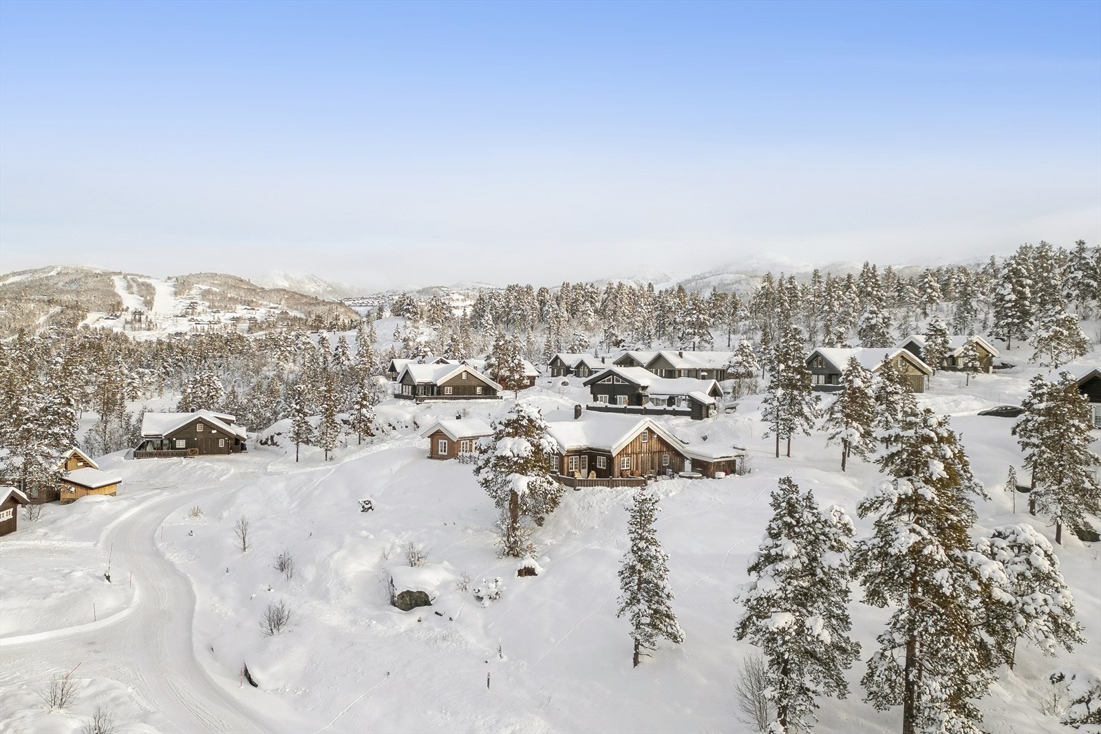 Dronebilde som viser hyttens plassering i et solrikt og etablert hyttefelt på Hovdeli. Galleribilde