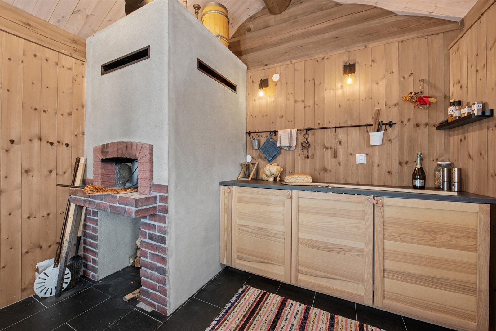 Kjøkkeninnredning med bakeovn/peis, flislagt gulv med varmekabler og praktiske arbeidsflater. Galleribilde