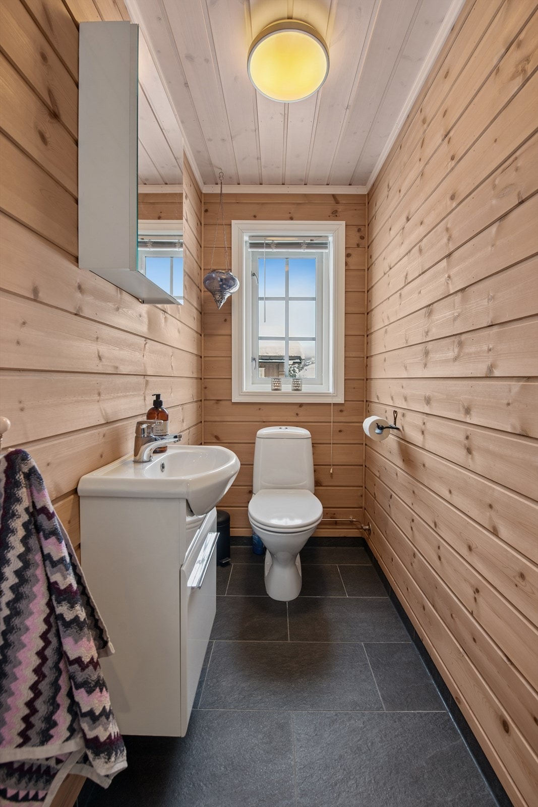 Separat gjestetoalett med flislagt gulv, panelte vegger og ventilasjon i himling. Galleribilde