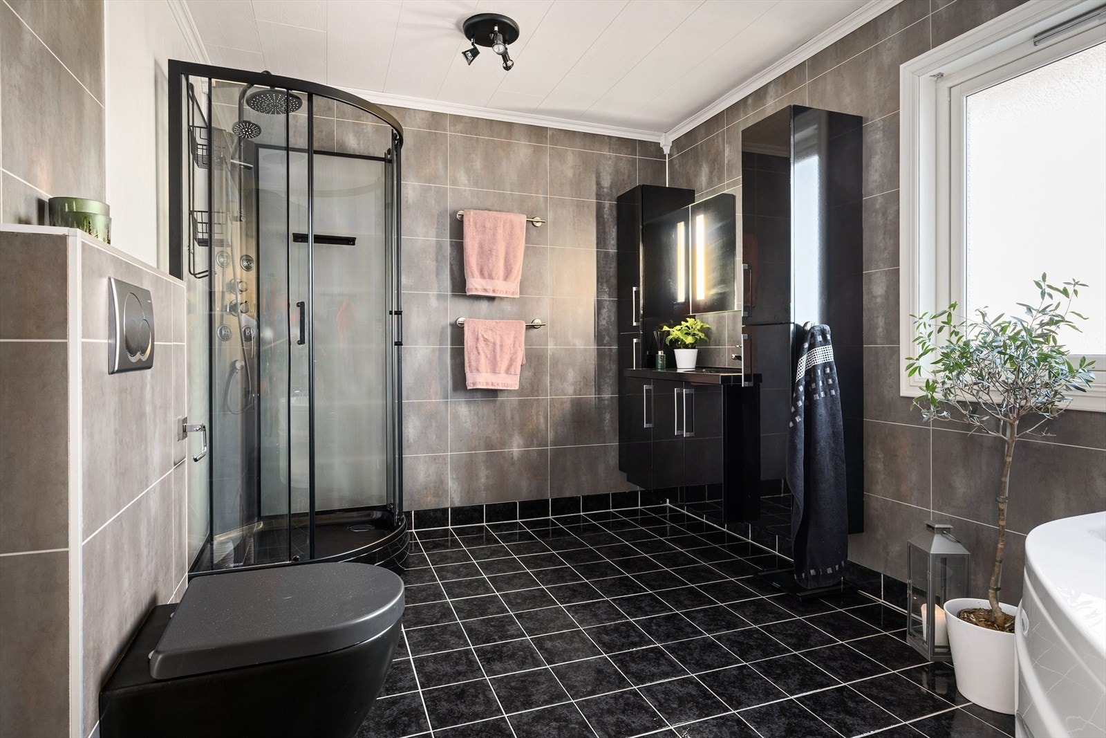 Badet har badekar, dusjkabinett med regnfallsdusj, servant med innredning, høyskap og vegghengt wc. Galleribilde