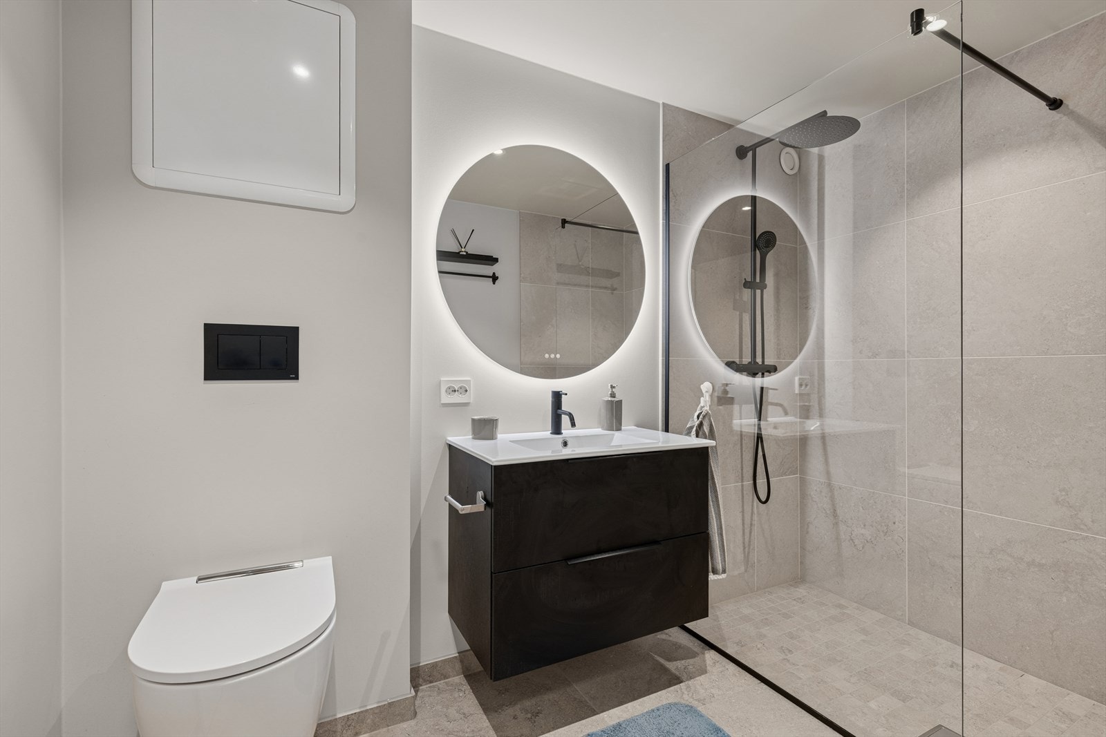 Lekkert bad med dusj nisje, servant med underskap, vegg hengt toalett og speil med belysning. Rør i rør. Galleribilde