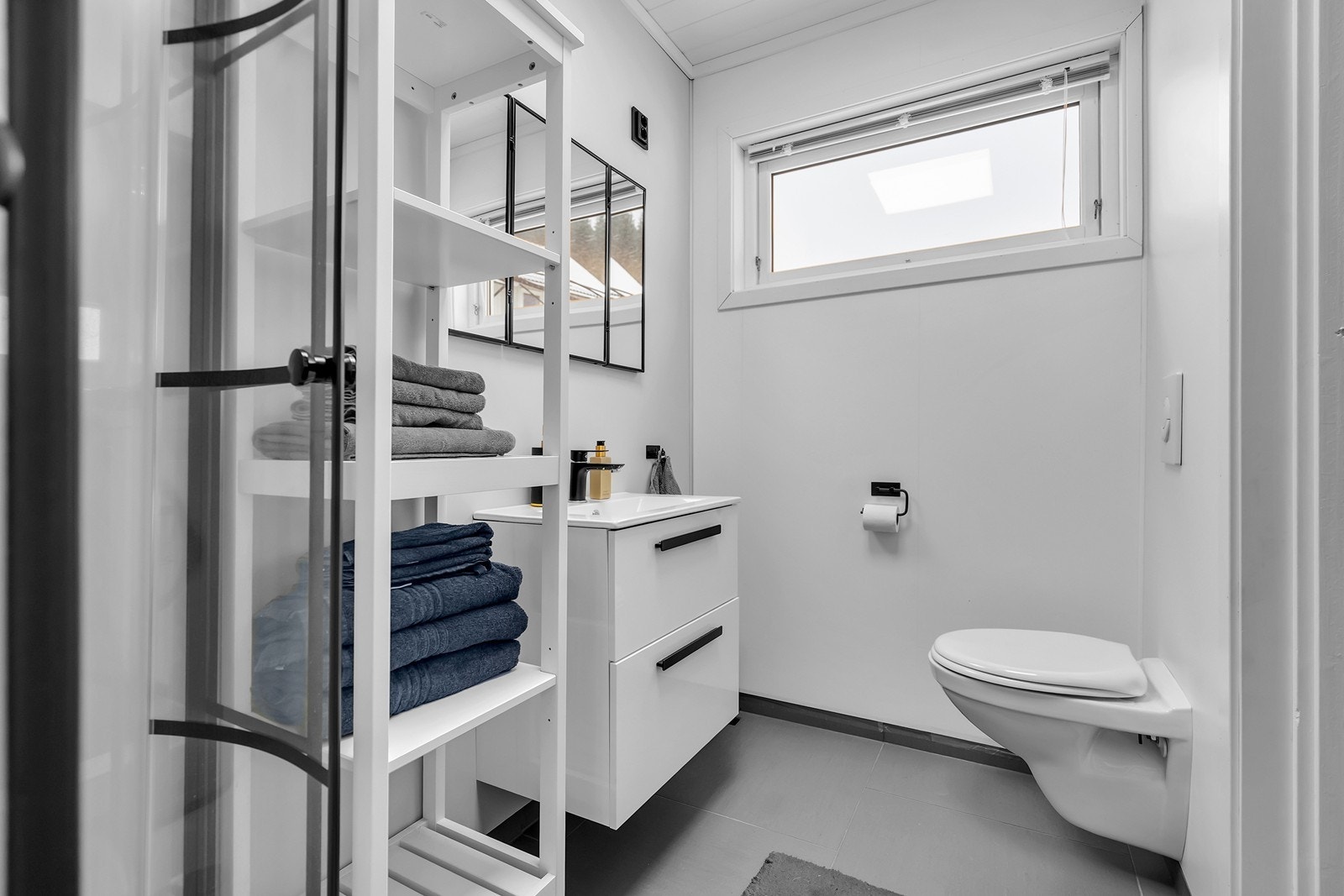 Rommet er innredet med dusjkabinett, innredning med vask og speil, vegghengt toalett og elektrisk vifte. Galleribilde