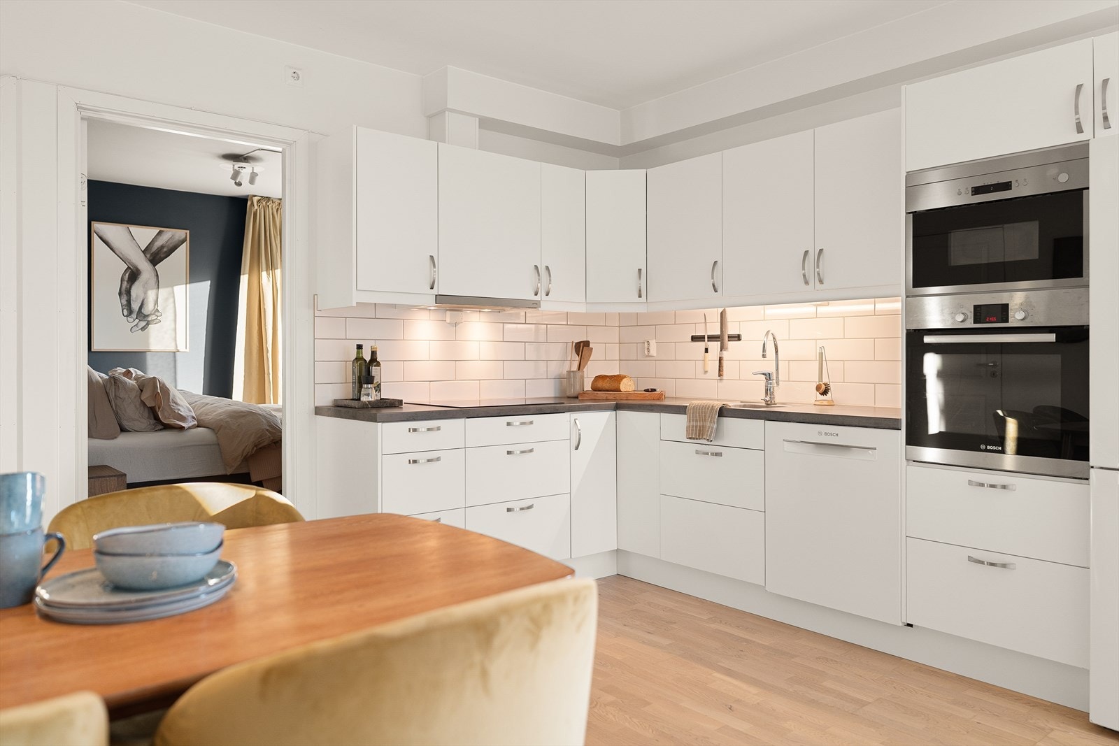 Kjøkkeninnredning med lyse glatte fronter og fliser på vegg over laminert benkeplate. Galleribilde