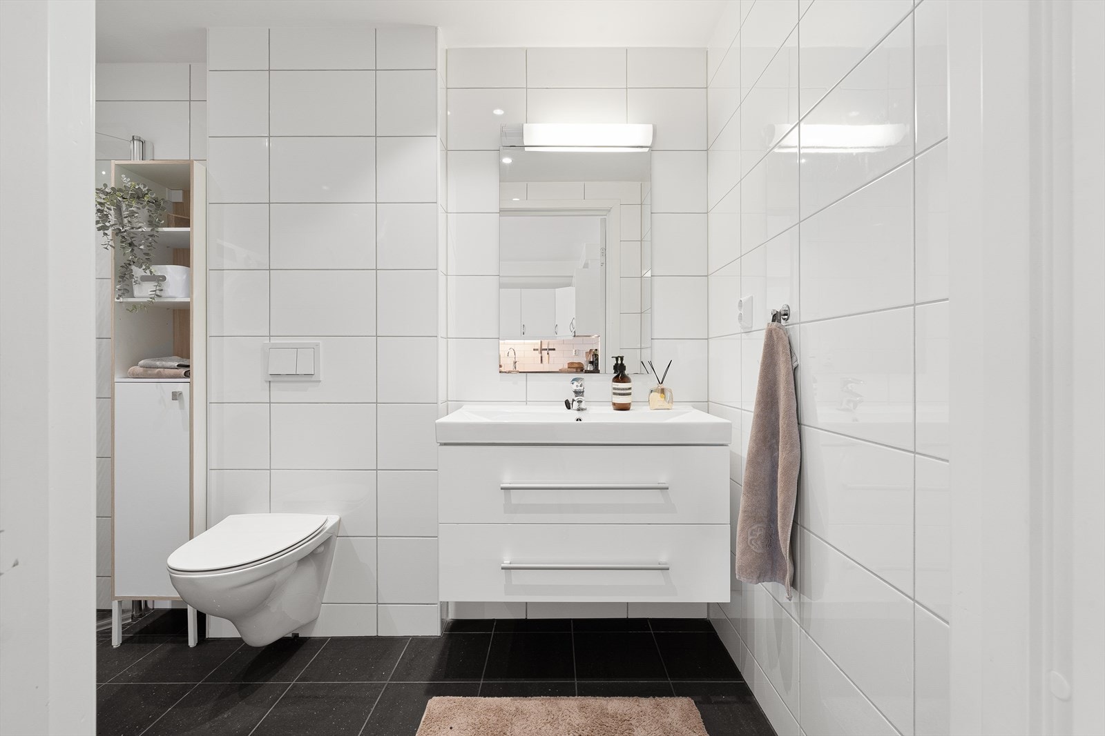 Pent helfliset bad innredet med baderomsinnredning med servant, vegghengt toalett, dusj og opplegg for vaskemaskin. Galleribilde