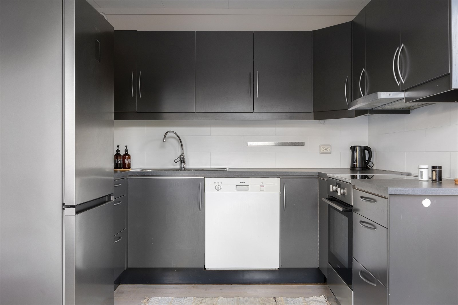 Kjøkkenet har et praktisk og stilrent design med slette fronter og en benkeplate av laminat med nedfelt vask. Mellom benkeplaten og veggskapene er det fliser som gir et moderne preg. Galleribilde