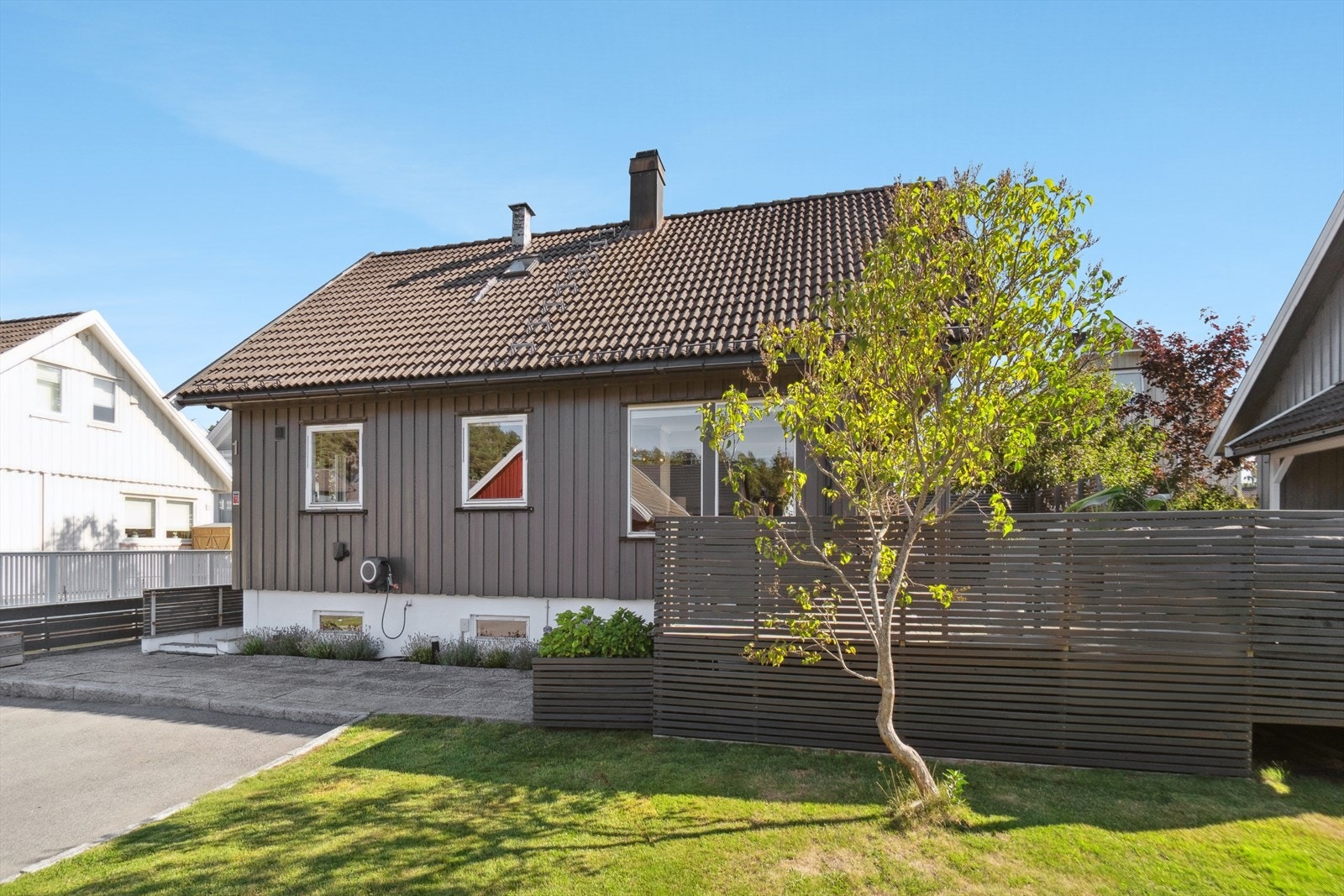 Tomten er pent opparbeidet med steinheller, plen, trær og annen beplantning. Galleribilde