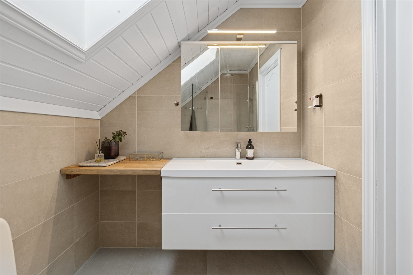 Flislagt baderom som er innredet med dusjhjørne, servant med skapinnredning og toalett. Galleribilde