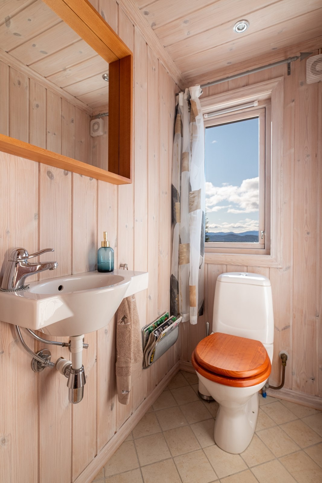 Praktisk toalettrom som inneholder gulvmontert toalett, servant og speil. Overflater består av flis på gulv med varmekabler, panel på vegg og panel i himling med spotter. Galleribilde