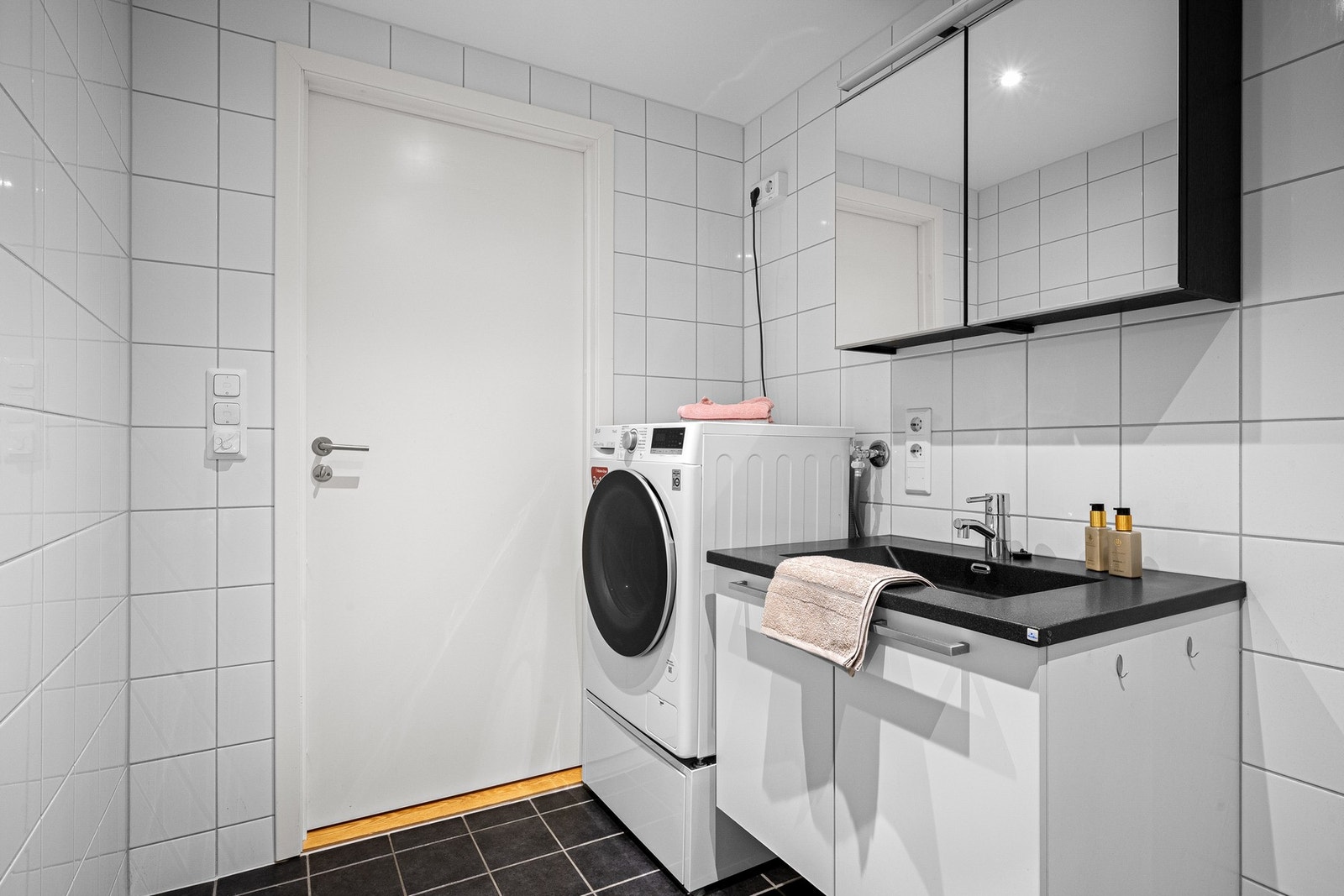 Badet er praktisk innredet med seksjon med servant og oppbevaringsskap, speilskap, dusj og opplegg for vaskemaskin Galleribilde