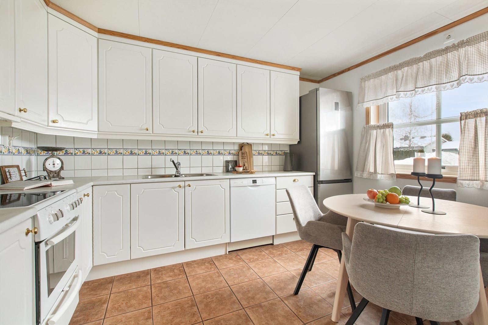 Kjøkkenet har profilerte fronter og laminerte benkeplater med fliser mellom benk og overskap. Galleribilde