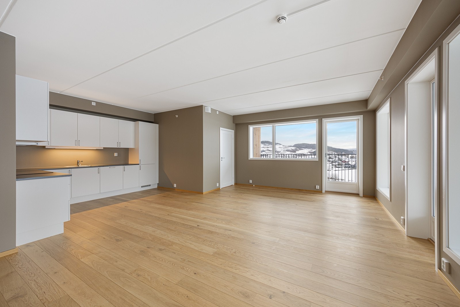 Stue og kjøkken i åpen løsning danner et sosialt allrom, samtidig som kjøkkenet er litt tilbaketrukket Galleribilde