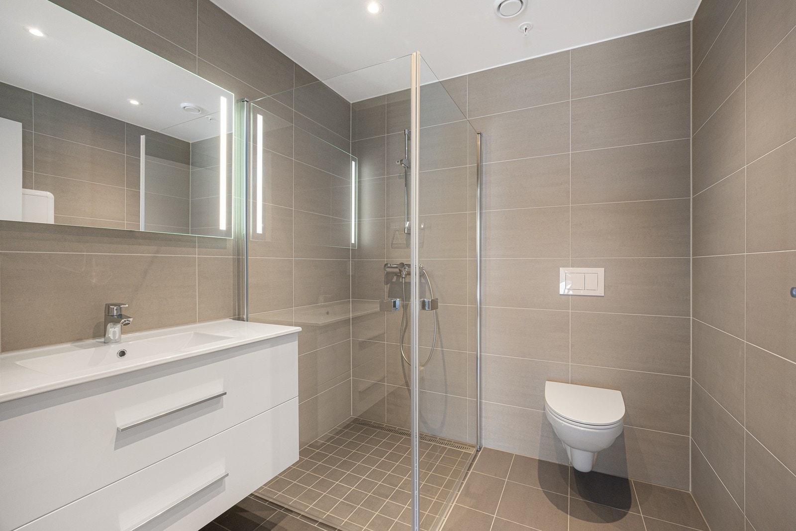 Bad ved hovedsoverommet. Grå fliser på badene gir et lunt uttrykk. Det er downlights i taket og elektriske varmekabler i gulvet Galleribilde