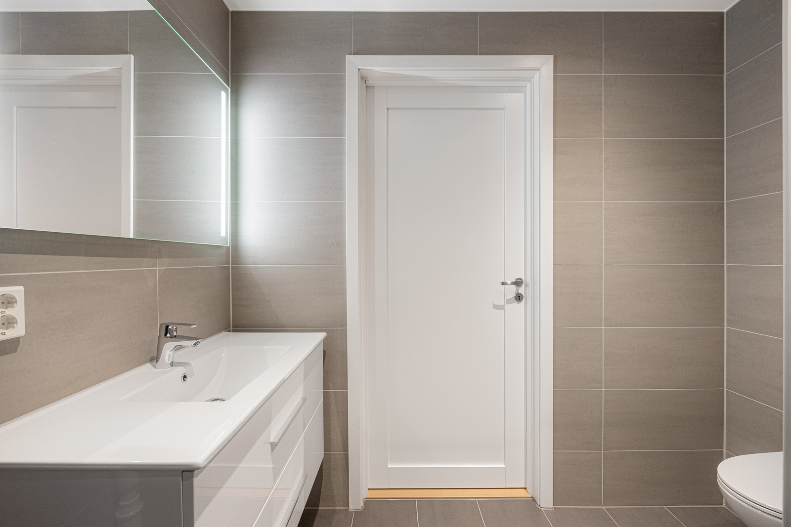 Baderomsinnredning med skuffer i hvit utførelse med glatte fronter, heldekkende servant, ett-greps batteri og tilhørende speil med lys Galleribilde