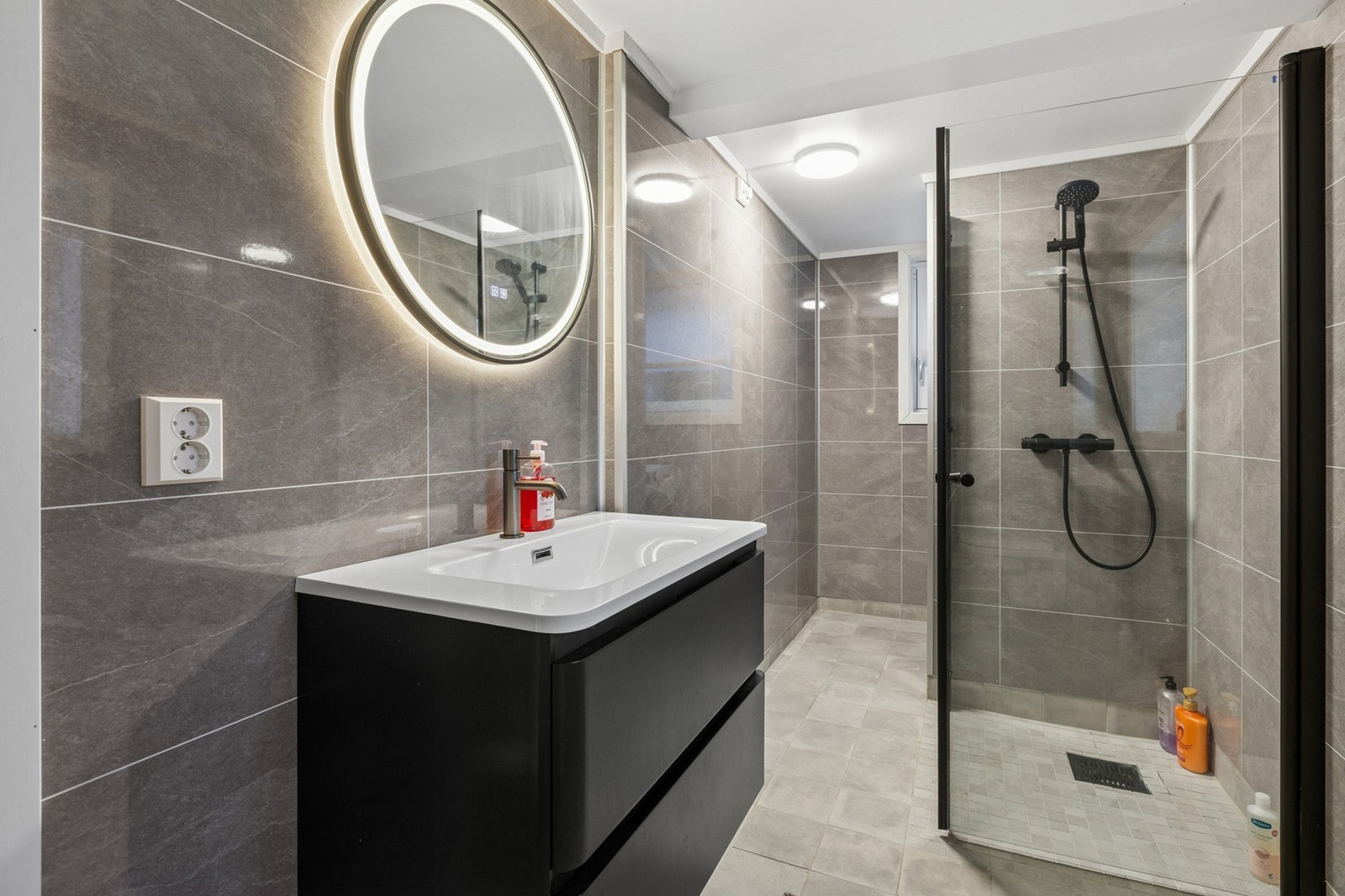 Delikat og moderne bad med flislagt gulv med varme og vegghengt servantskap med heldekkende servant. Galleribilde