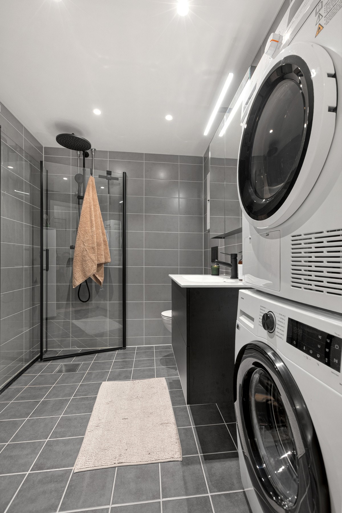 Innredningen består av servant med underskap, belyst speilskap, vegghengt WC og en romslig dusjsone med innfellbare dører av herdet glass med regnfall-dusjhode Galleribilde