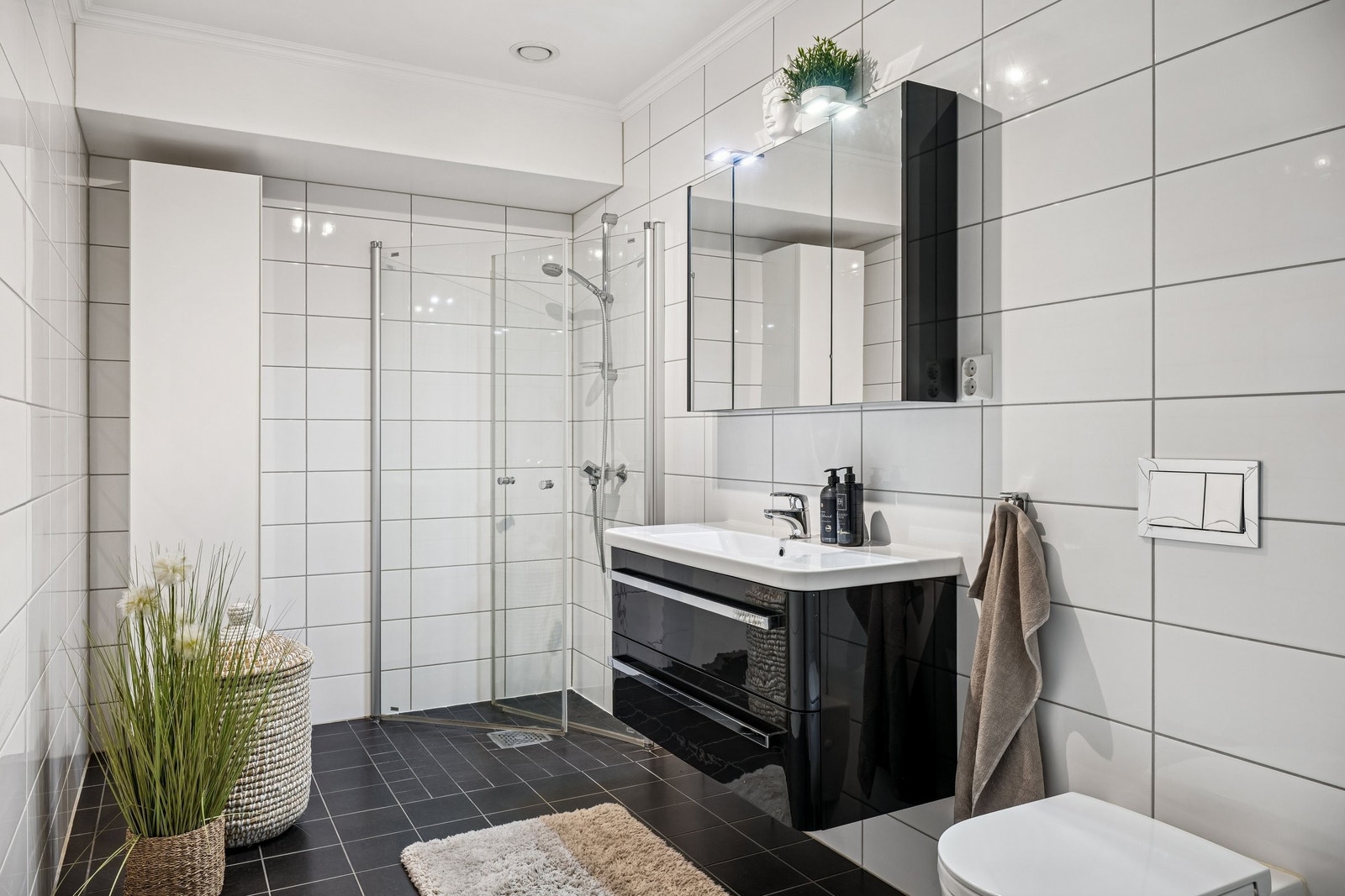 Flislagt bad med innredning og nedfelt servant, veggmontert toalett og dusjhjørne med glassvegger. Praktisk høyskap med hyller. Elektriske varmekabler i gulv og malt betonghimling. Galleribilde