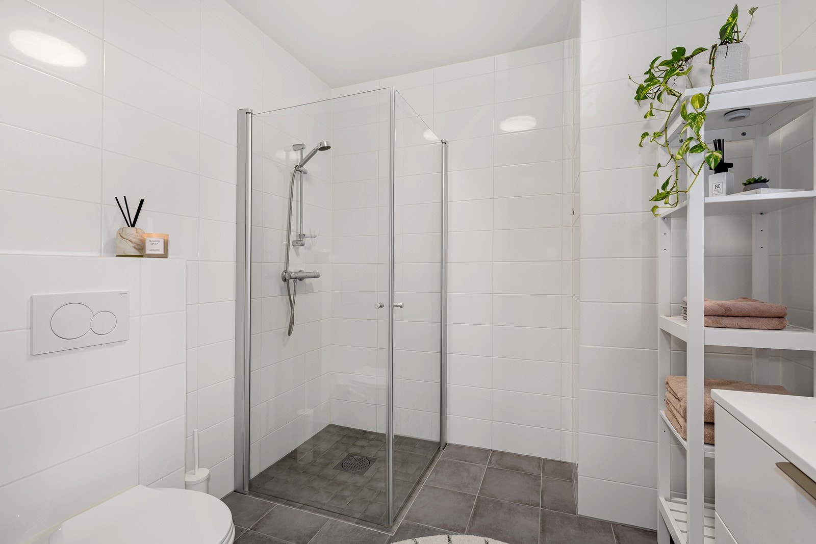 Lyst og pent bad med vegghengt toalett og dusjhjørne i glass. Galleribilde