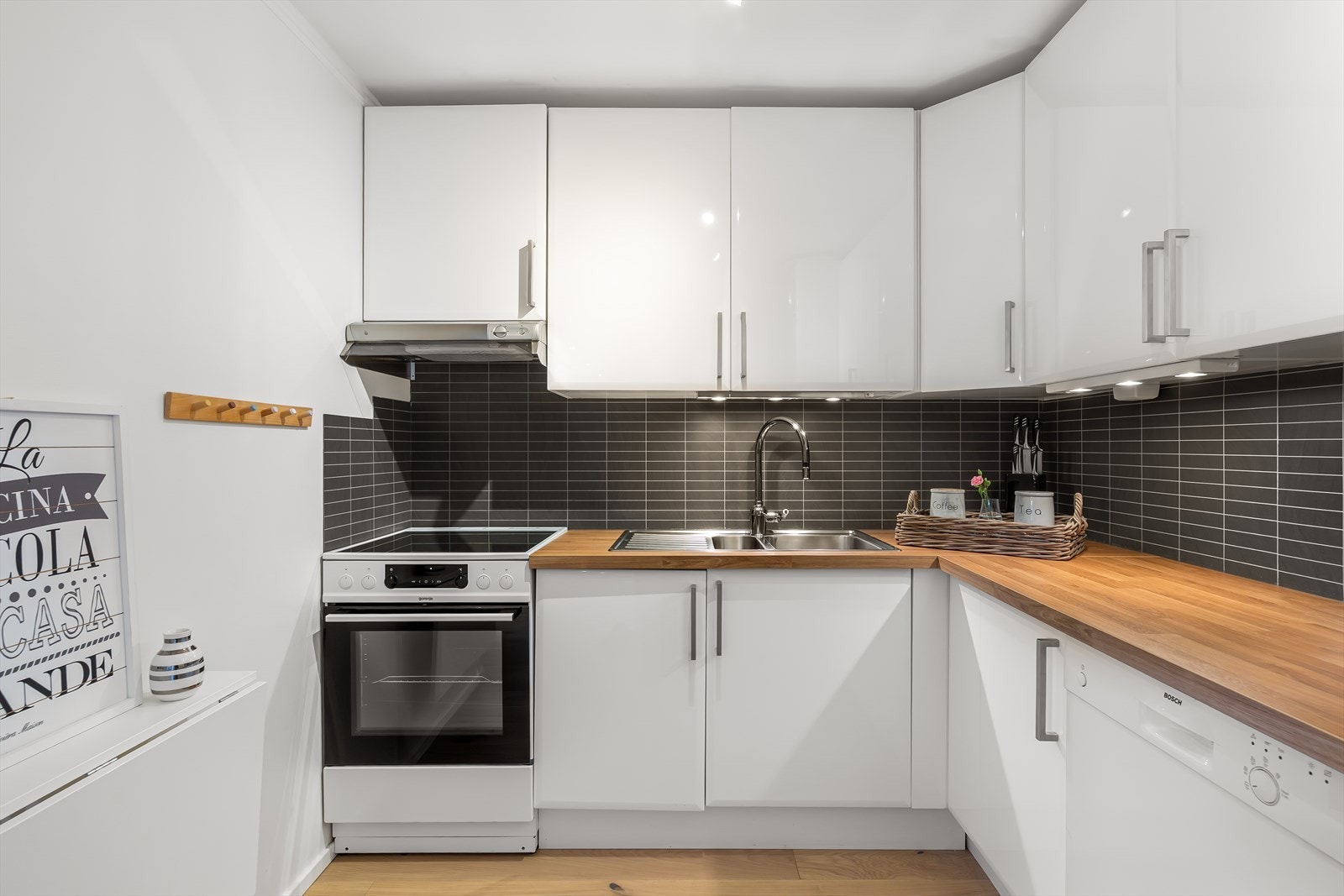 Praktisk kjøkken i delvis åpen løsning mot stuen, med moderne innredning med glatte fronter. Under overskapene er det integrert belysning og veggen over benkeskapene er beskyttet med stilrene plater Galleribilde