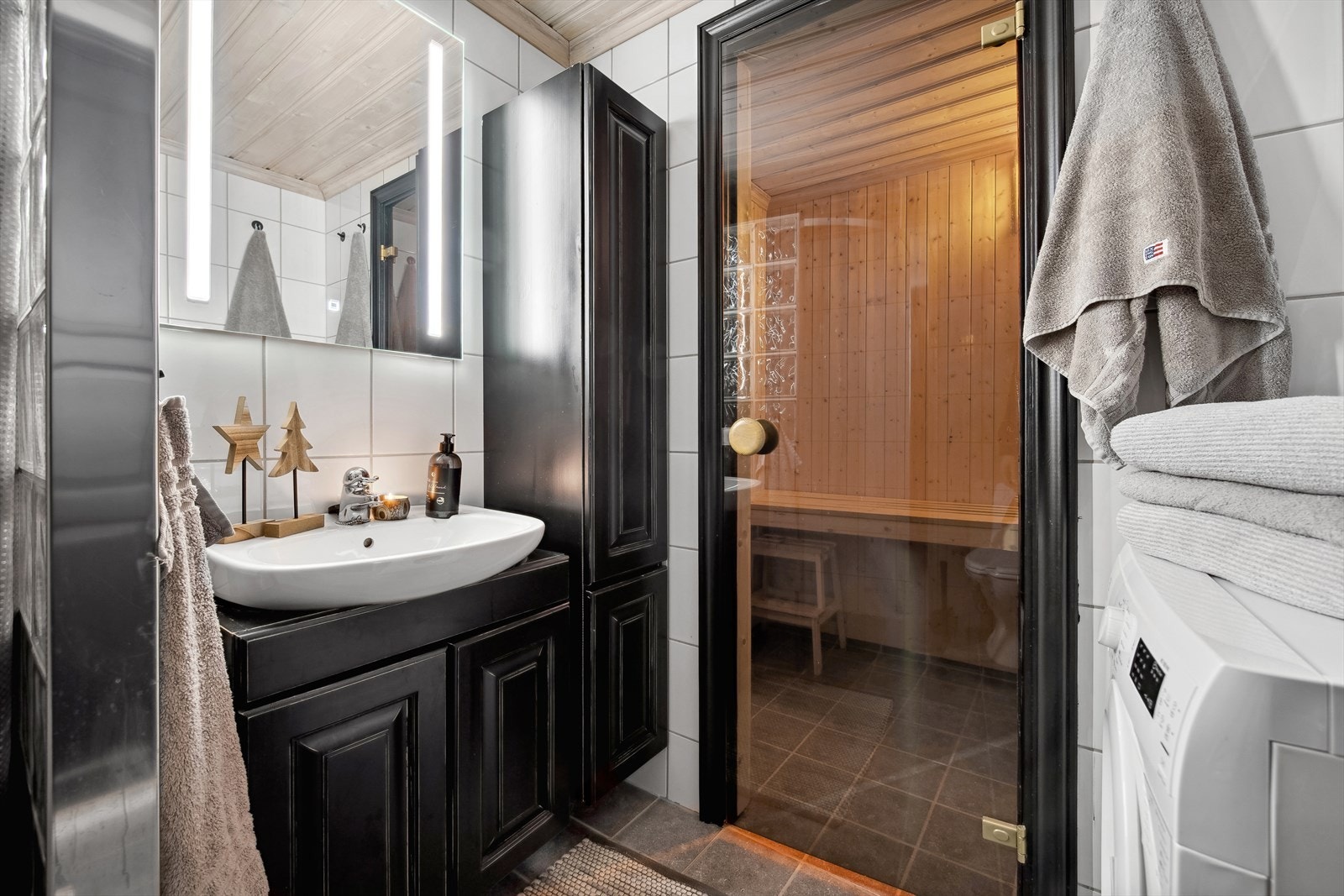 Badet er funksjonelt og gjennomtenkt, med innredning som inkluderer speil, servant med møbel, toalett og dusjnisje. Det er også opplegg for vaskemaskin, samt direkte inngang til badstue - perfekt for en avslappende dag. Galleribilde