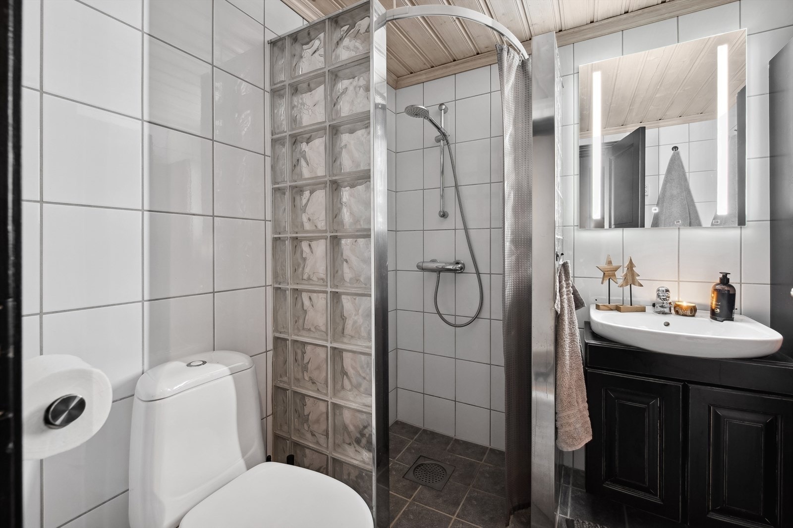 Badet har fliselagte vegger og gulv som gir et stilrent og lettstelt uttrykk. Baderomsinnredningen er fra samme leverandør som kjøkkenet, noe som gir en gjennomført og lekker hyttestil i hele leiligheten. Galleribilde