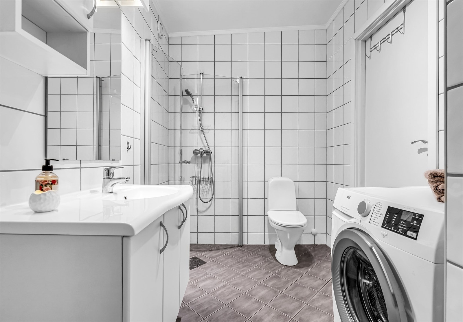 Lyst flislagt bad med gulvvarme. Innredningen består av gulvstående toalett og vegghengt servantinnredning med ovenpåliggende vask. Galleribilde