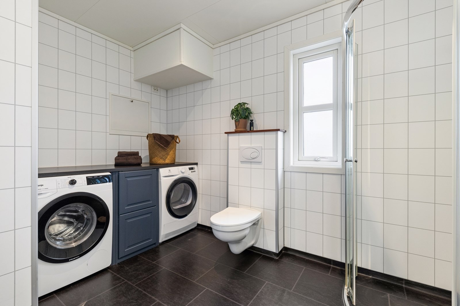 Badet er ellers utstyrt med dusjhjørne, vegghengt toalett og baderomsinnredning med god lagringsplass og nedfelt servant. I tillegg har man opplegg for vaskemaskin og plass til tørketrommel med gode arbeidsflater på benk over. Galleribilde
