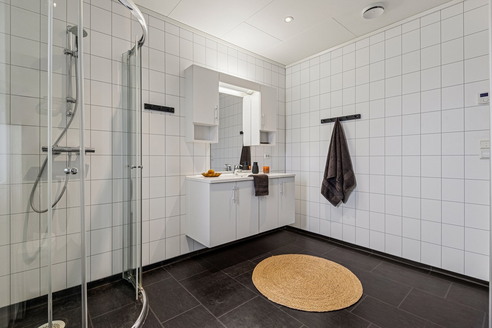 Baderommet er tidløst innredet med mørk vinylbelegg på gulv og hvite baderomsplater på vegg. I gulvet har man også varmekabler for ekstra komfort. Galleribilde