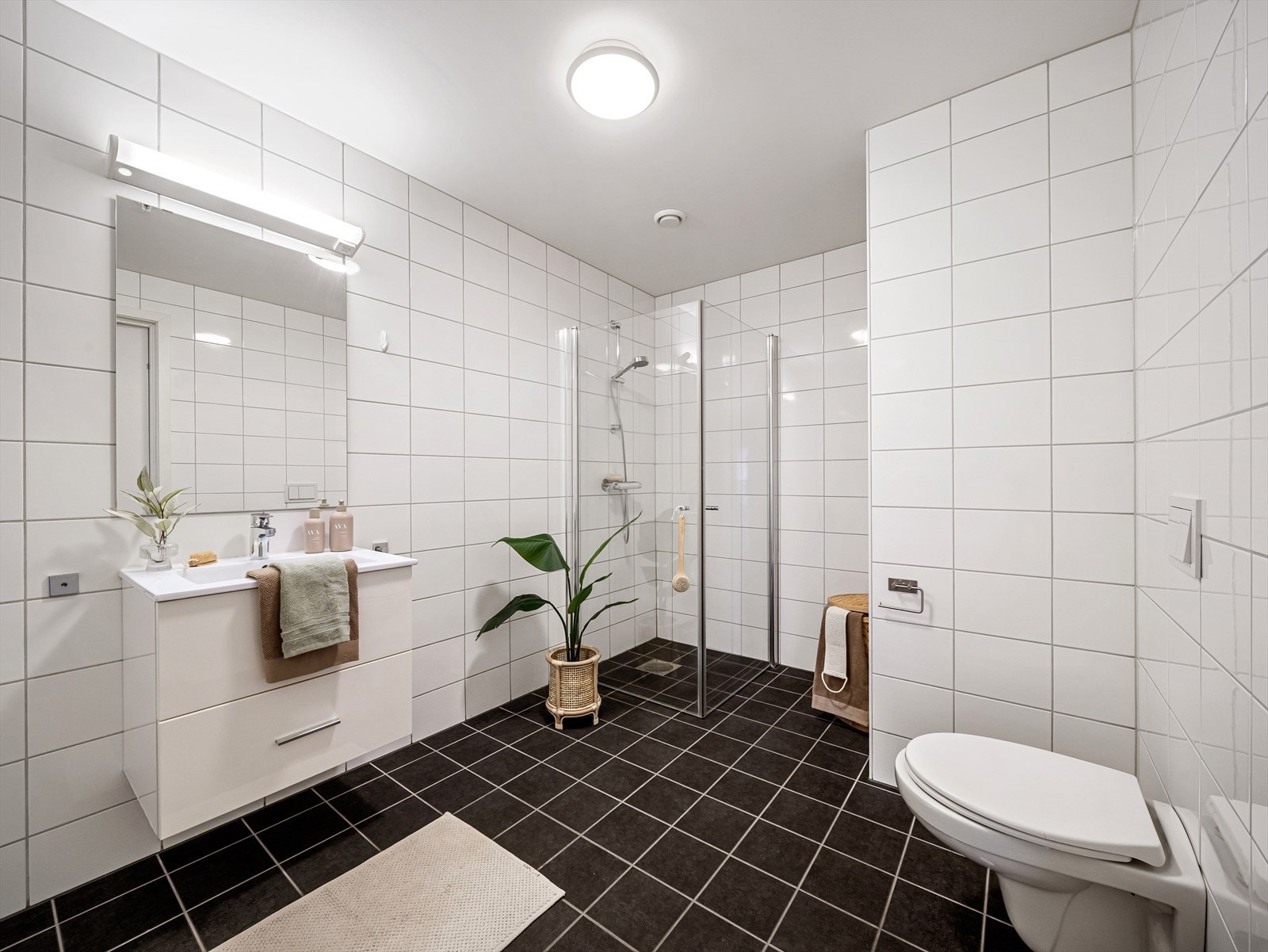Badet er romslig og har en praktisk og funksjonell innredning bestående av vegghengt toalett, servant med underskap, speil med belysning, dusjhjørne og nisje til vaskemaskin/tørketrommel. Galleribilde