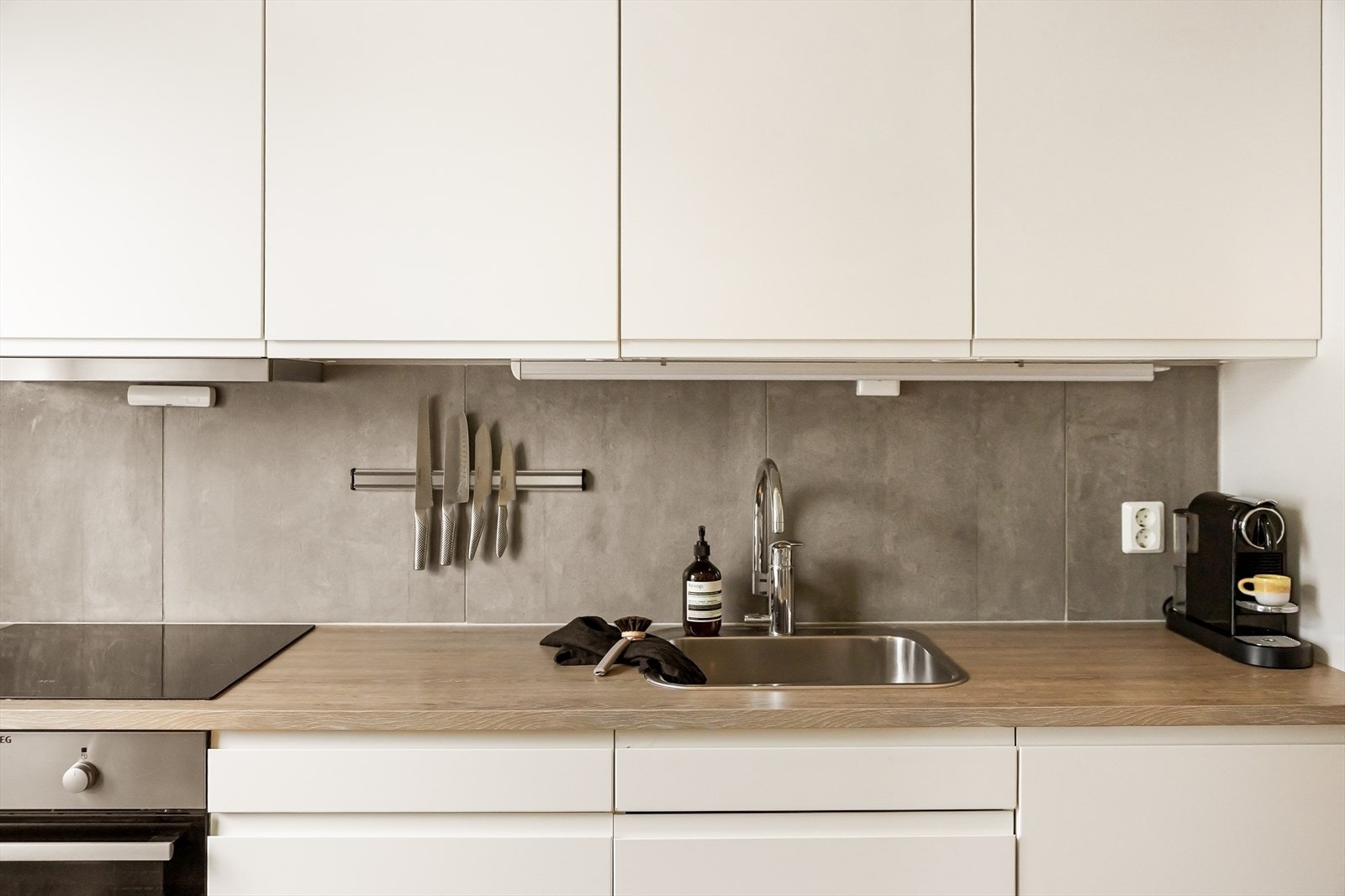 Kjøkkeninnredningen fra Norema strekker seg langs den ene veggen og har en moderne fremtoning med hvite, glatte fronter og benkeplate i laminat som står i stil med gulvet. Galleribilde