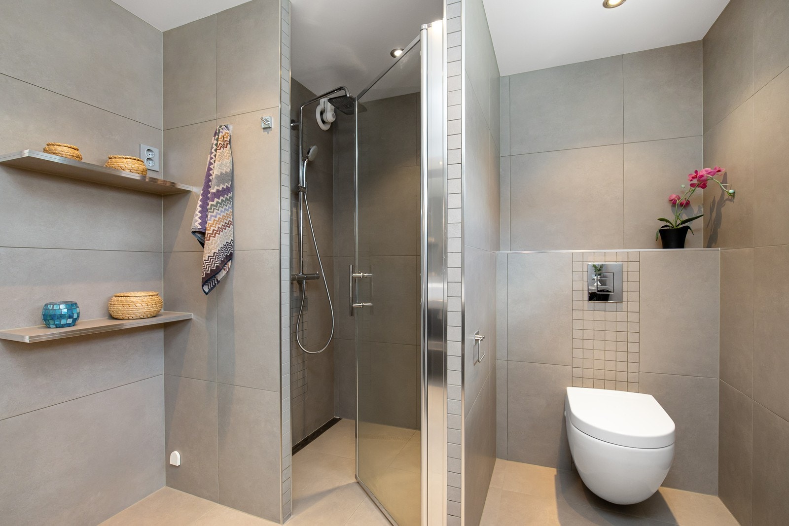 Dusjnisje med flislagte hjørnehyller og glassdør. Vegghengt toalett med utenpåliggende sisterne Galleribilde