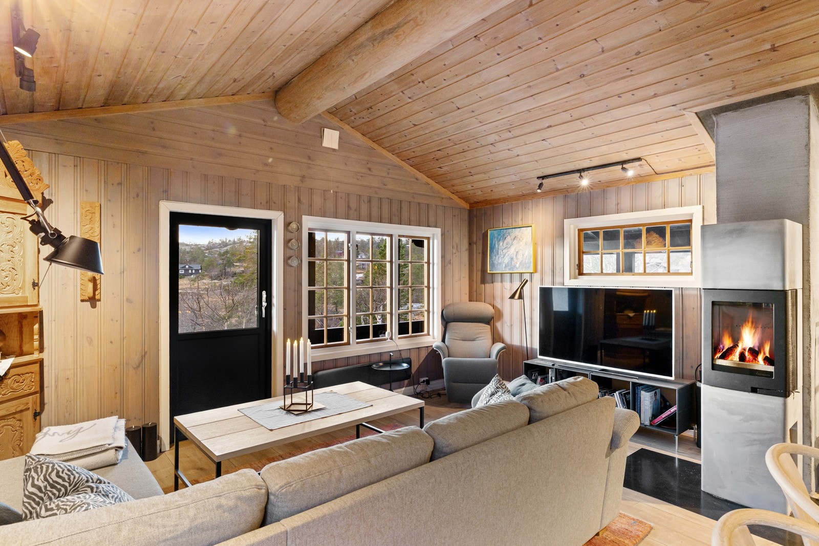 Stuen har gjennomgående trepanel på vegger og himling, kombinert med generøs takhøyde og synlige konstruksjonselementer som gir et varmt og karakterfullt hyttepreg. Galleribilde