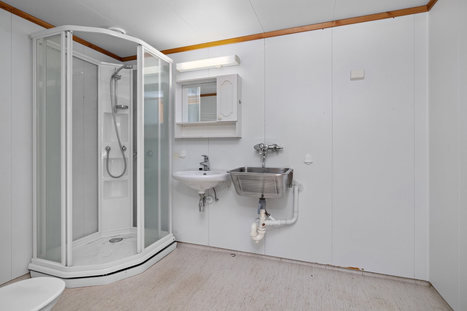 Badet er et kombinert bad/wc og vaskerom med dusjkabinett, servant og utslagsvask, badet er fra byggeår Galleribilde