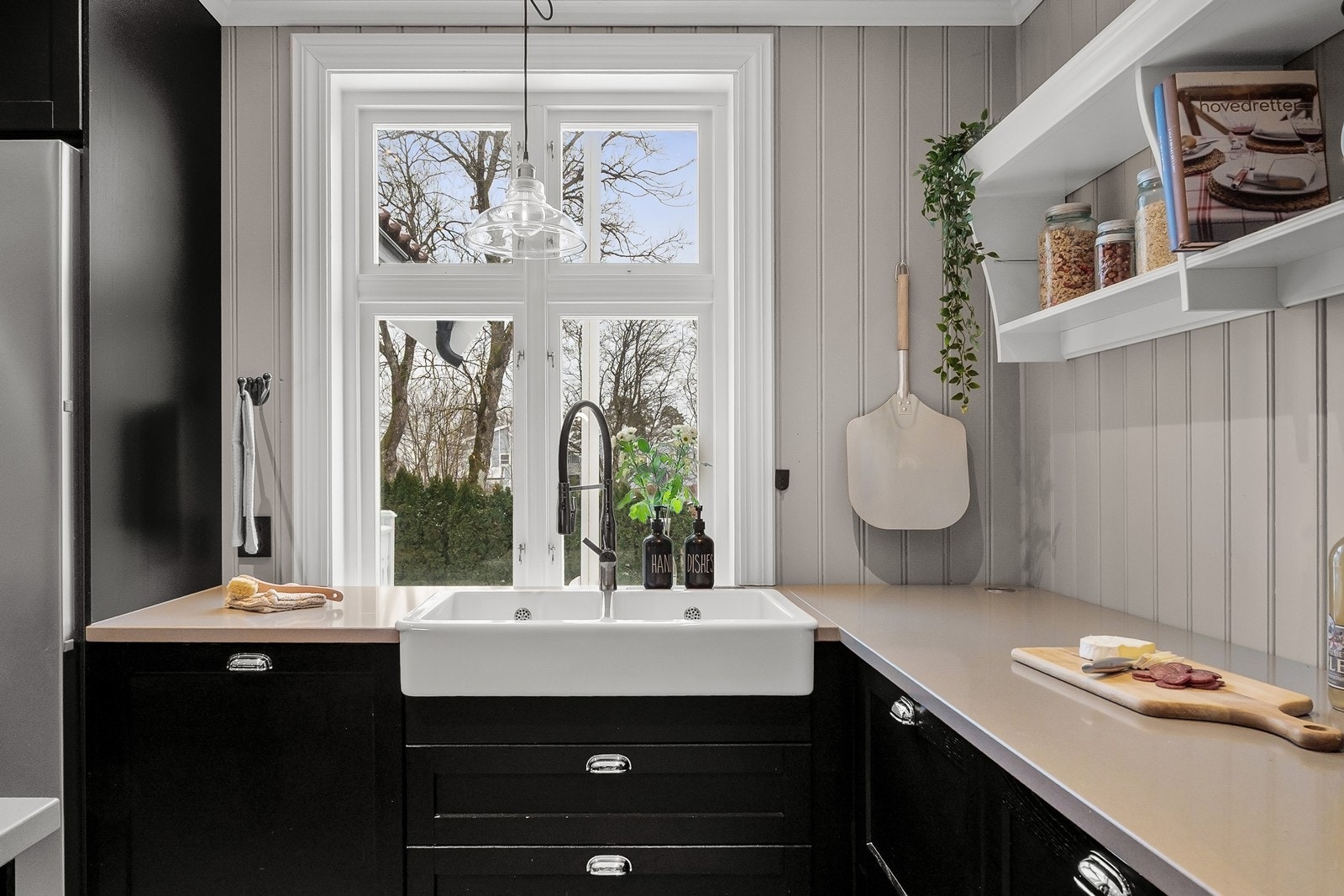 Langs vindusveggen er det dobbel oppvaskkum med utsyn mot hagen, og over benken er det åpne hyller som gir rom for både oppbevaring og dekor. Galleribilde