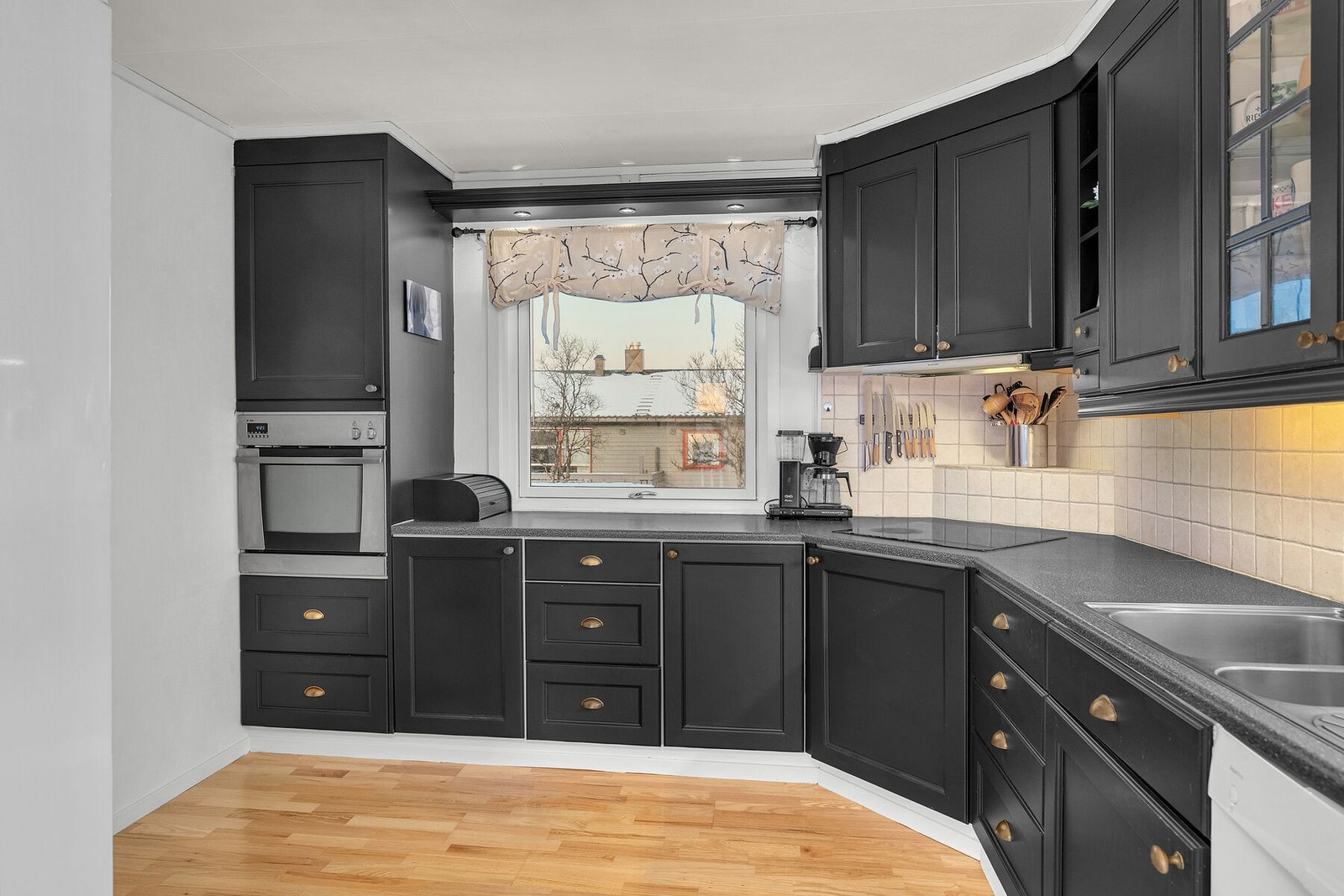 Kjøkken med malte, profilerte fronter og laminat benkeplate. Det er integrert komfyr og platetopp, samt nisje for oppvaskmaskin og kjøleskap. Galleribilde